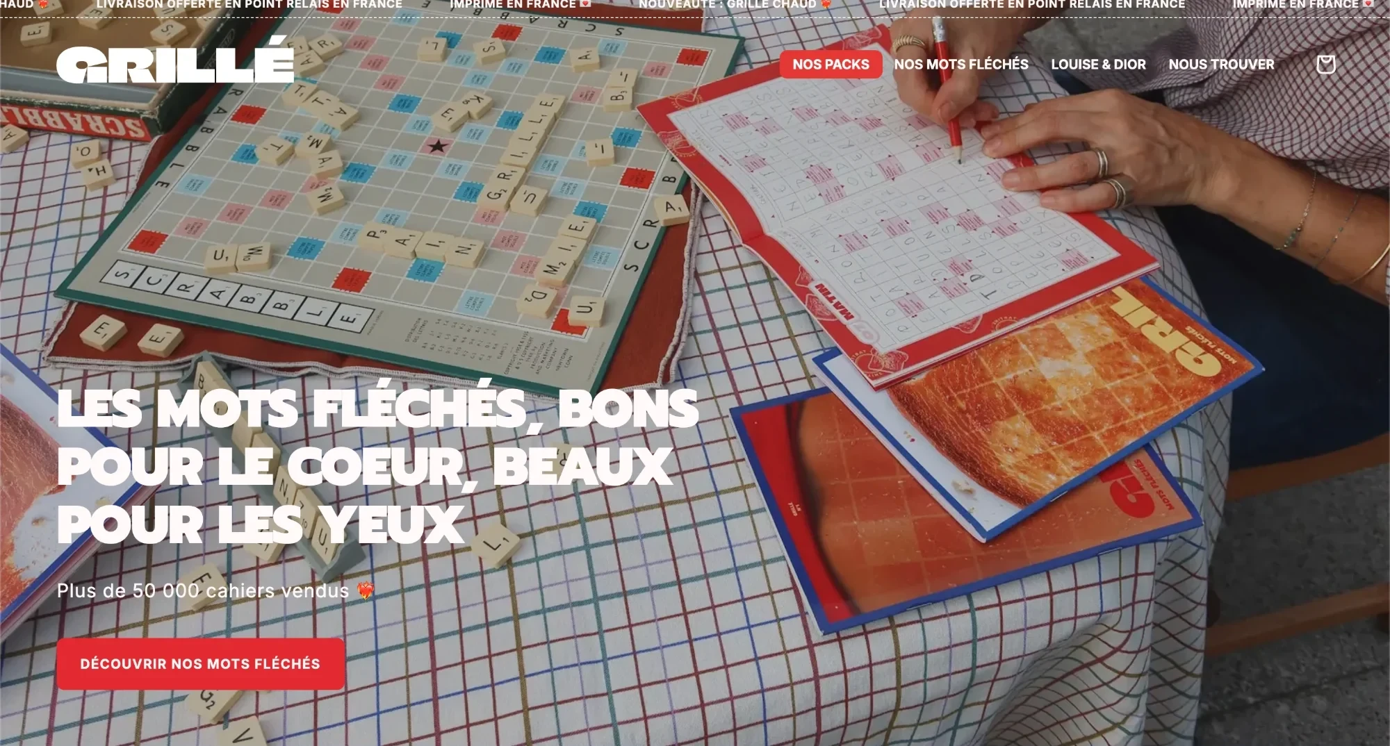 The Grillé home page: a booklet of arrow words being filled in with a red pencil on a checked tablecloth, beside a Scrabble board, under the headline Les mots fléchés, bons pour le coeur, beaux pour les yeux.